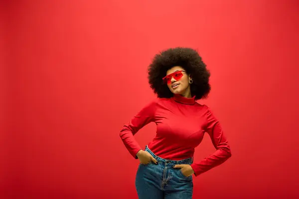 Stylish African American woman wearing a red shirt with a red heart on her face poses against a vibrant backdrop. — Stock Photo