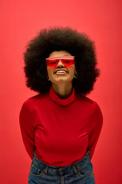 Stylish African American woman in red glasses and shirt posing on vibrant backdrop. — Stock Photo