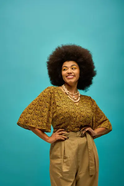 Femme afro-américaine élégante avec cheveux bouclés debout devant un fond bleu vibrant. — Photo de stock