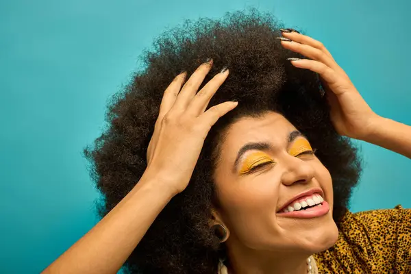 Una mujer afroamericana con estilo y sombra de ojos de color amarillo brillante posa sobre un vibrante telón de fondo. - foto de stock