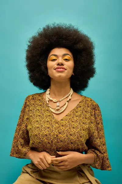 Stylish African American woman with curly hairdositting on a chair in trendy attire against a vibrant backdrop. — Stock Photo