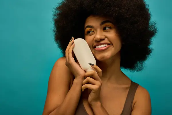 Stylish African American woman holding a hair dryer in front of her face on a vibrant backdrop. — Stock Photo