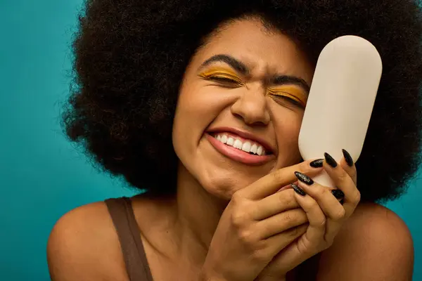 A stylish African American woman holds brush to her face against a vibrant backdrop. — Stock Photo