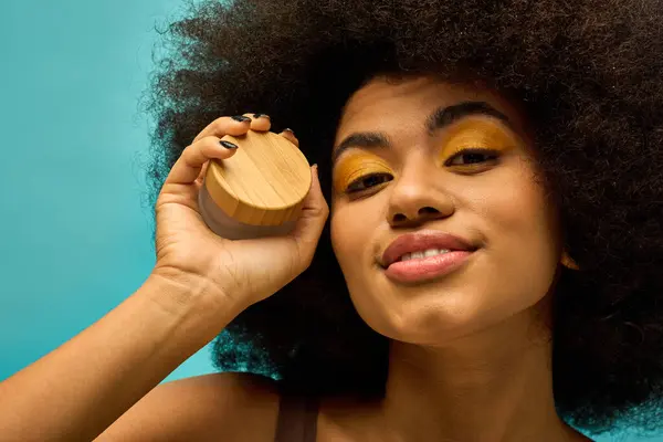 Femme afro-américaine élégante tenant la crème face à face dans une tenue à la mode sur fond vibrant. — Photo de stock