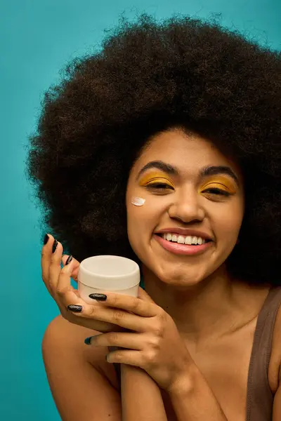 Trendy African American woman with curly hairdoholding cream jar. — Stock Photo