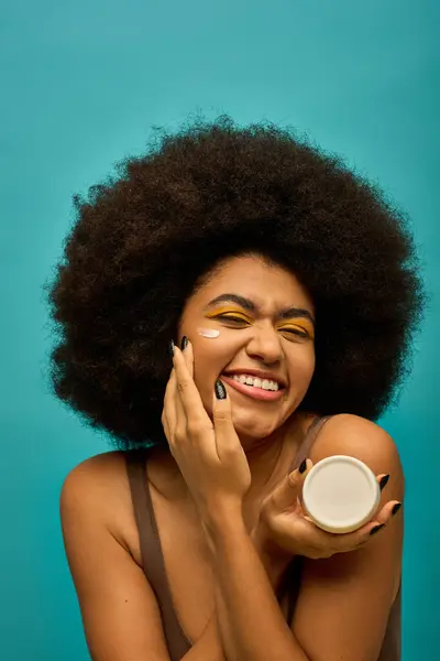Stylish woman with curly hairdo holding cream, posing against a colorful backdrop. — Stock Photo