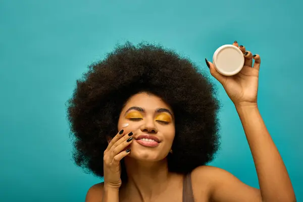 Stylish African American woman with curly hairdoholding cream. — Stock Photo
