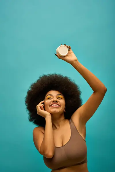 Elegante mujer afroamericana sosteniendo crema con su icónico peinado afro. - foto de stock