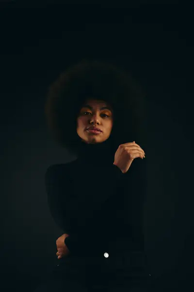 A fashionable African American woman with curly hairdostands confidently in the dark. — Stock Photo