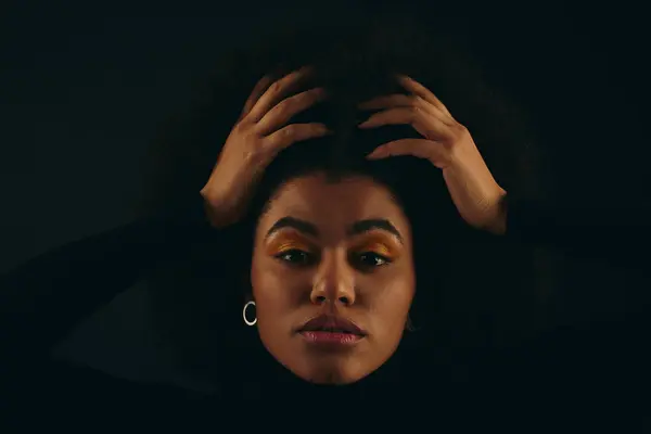 Una donna afroamericana elegante con le mani sulla testa in abiti alla moda su uno sfondo vibrante. — Foto stock