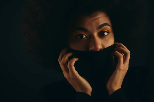 African American woman stylishly covers face with black cloth against vibrant backdrop. — Stock Photo