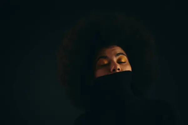 Femme afro-américaine avec les yeux fermés dans l'obscurité, tenue élégante. — Photo de stock
