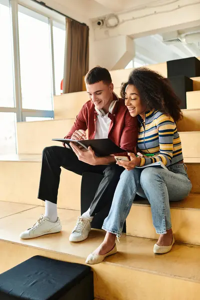 A man and a woman, students, sitting together on stairs in a multicultural setting, university or high school — Stock Photo