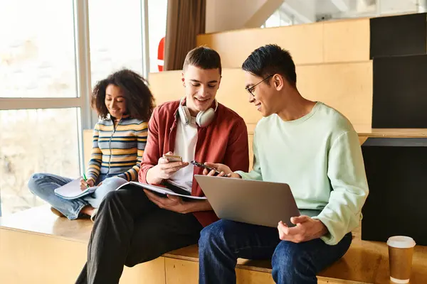 Three people of different ethnicities sitting on a counter, focused on a laptop screen in an educational setting — Stock Photo