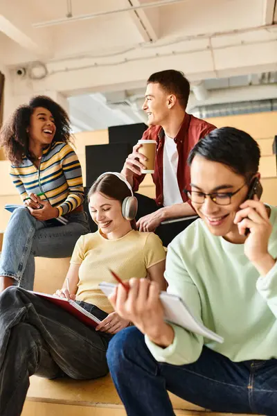 Un grupo diverso de estudiantes absortos en conversaciones telefónicas celulares mientras están sentados en los escalones - foto de stock