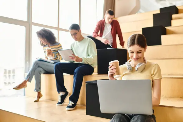 Groupe multiculturel de jeunes assis dans les escaliers, concentrés sur les ordinateurs portables, engagés dans l'apprentissage numérique — Photo de stock