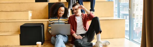 Um homem e uma mulher de diferentes origens étnicas sentam-se nas escadas, envoltos em uma tela de laptop, contemplando seu futuro compartilhado. — Fotografia de Stock