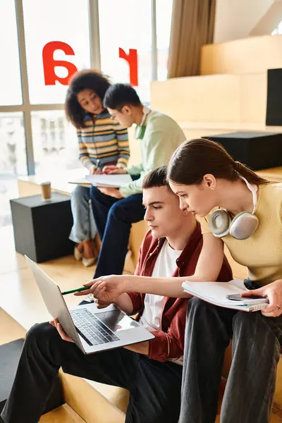 Multicultural group of students seated on bench, engrossed in laptops, working and collaborating in indoor setting. — Stock Photo