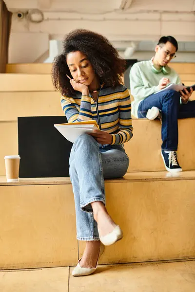 A woman, seated on a stage, engrossed in her tablet screen, immersed in technology and learning. — Stock Photo