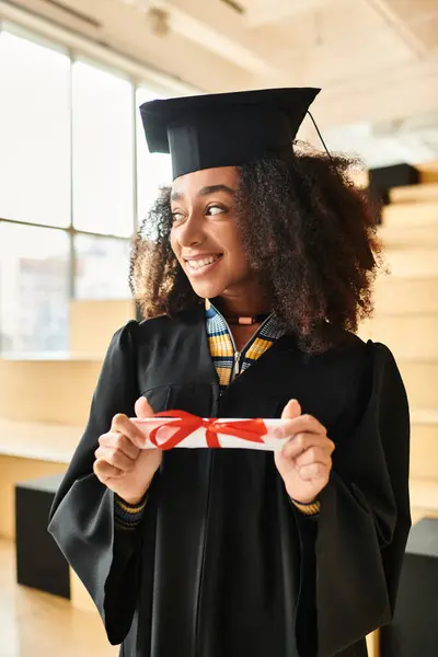 Una mujer afroamericana con una gorra de graduación y un vestido, celebrando su logro académico. - foto de stock