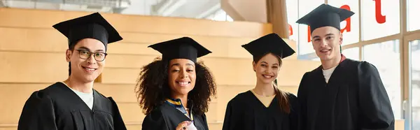 Мультикультурная группа студентов в выпускных шапках и платьях празднует академический успех в помещении. — стоковое фото