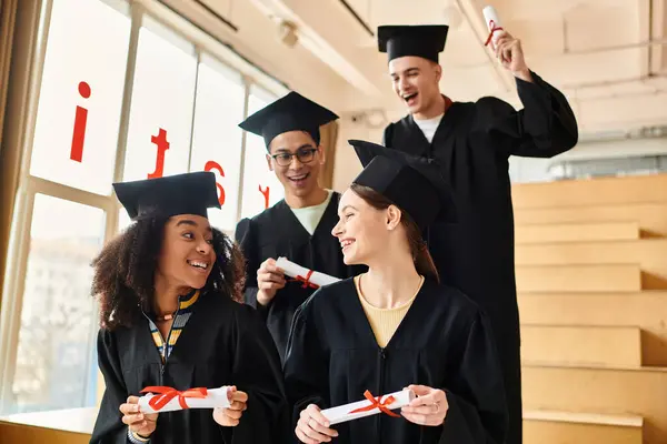 A group of diverse students in graduation gowns holding diplomas, smiling in celebration of their academic accomplishments. — Stock Photo