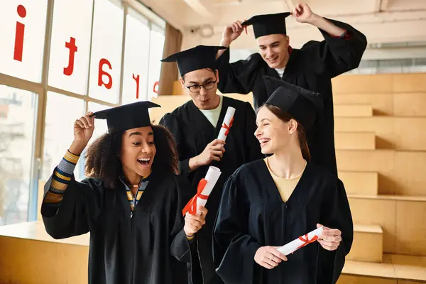 Un grupo diverso de estudiantes con batas de graduación y morteros señalando su éxito académico. - foto de stock