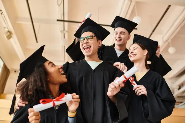 Grupo de estudiantes alegres con gorras de graduación y vestidos celebrando sus logros académicos en una ceremonia universitaria. - foto de stock