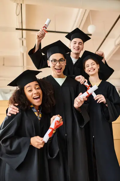 Різноманітна група студентів у випускних сукнях та академічних шапках посміхаються для зображення на честь своєї освітньої віхи. — стокове фото