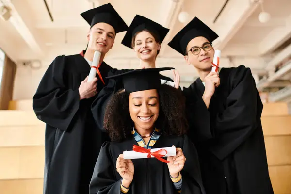 Diverso grupo de estudiantes felices en trajes de graduación y gorras posando para una foto de celebración en el interior. - foto de stock