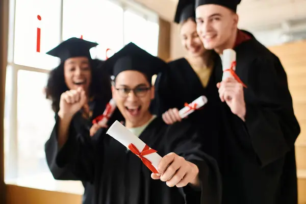 A diverse group of happy students in graduation gowns holding diplomas. — Stock Photo