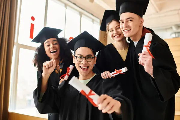 Un grupo diverso de estudiantes en trajes de graduación y gorras posando alegremente para una foto para conmemorar su éxito académico. - foto de stock