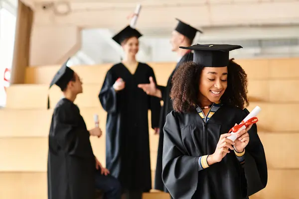 Um grupo diversificado de estudantes em vestidos de graduação, uma menina negra olhando para o seu diploma em emoção entre eles. — Fotografia de Stock