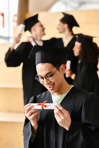 Un hombre diverso en un vestido de graduación alegremente sosteniendo su diploma. - foto de stock