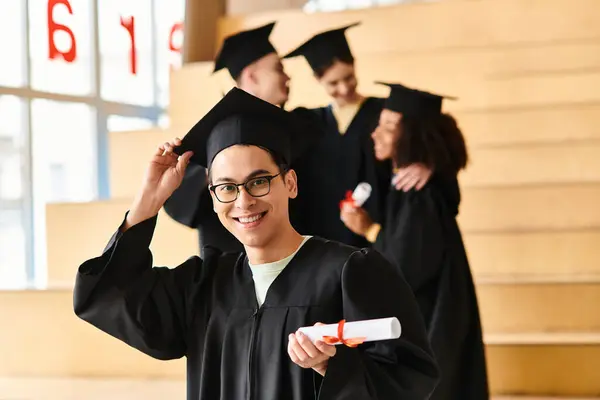 Un homme d'origines diverses célèbre l'obtention de son diplôme dans une casquette et une robe, affichant fièrement son diplôme. — Photo de stock