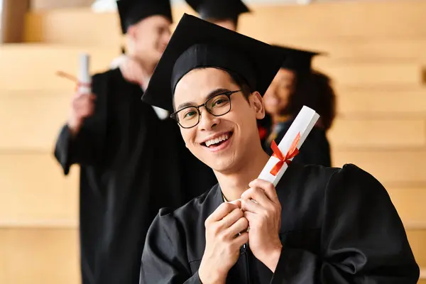 Un hombre feliz, representando la diversidad, graduándose en gorra y bata, con un diploma en la mano. - foto de stock