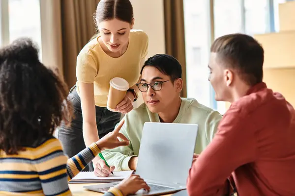 Un grupo diverso de estudiantes participan en la discusión y trabajan juntos usando una computadora portátil en una mesa en un entorno educativo. - foto de stock