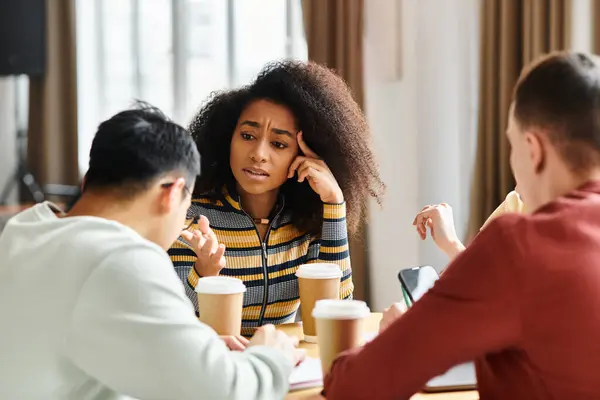 Um grupo diversificado de estudantes envolvidos em uma conversa animada em torno de uma mesa em um ambiente educacional. — Fotografia de Stock