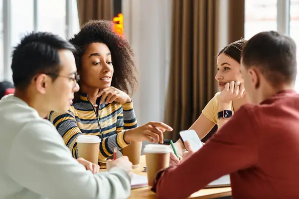 A diverse group of students from different backgrounds sit together, engaging in a lively discussion at a wooden table indoors. — Stock Photo