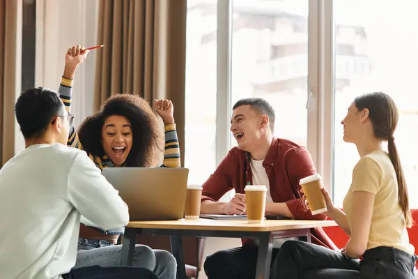 Um grupo multicultural de estudantes felizes trabalhando juntos em torno de uma mesa com um laptop em um ambiente educacional. — Fotografia de Stock