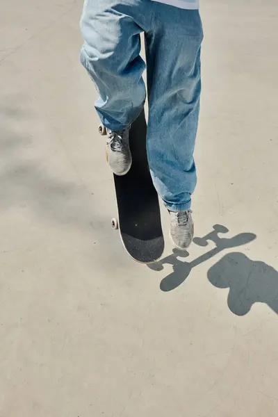 Un joven patinador monta elegantemente un monopatín sobre una superficie lisa de cemento en un vibrante parque de skate en un soleado día de verano.. - foto de stock