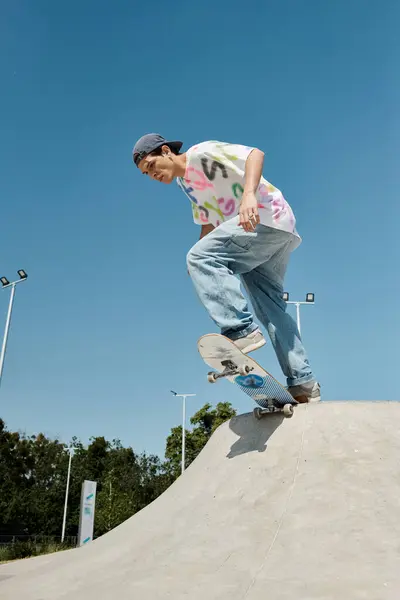Jeune patineur garçon monte courageusement sa planche à roulettes sur la rampe dans un skate park en plein air sur une journée d'été ensoleillée. — Photo de stock