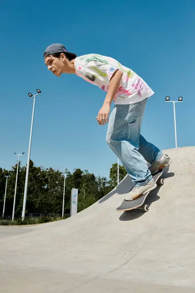 A young man glides effortlessly down the side of a ramp on his skateboard in a bustling outdoor skate park on a sunny summer day. — Stock Photo