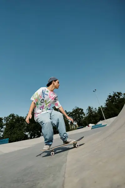 Un joven skater monta su monopatín sin miedo por el lado de una rampa en un animado parque de skate al aire libre en un día de verano.. - foto de stock