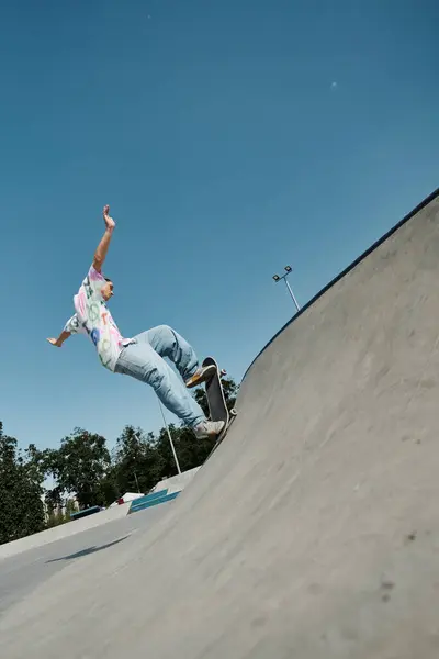 Un jeune patineur défie la gravité alors qu'il monte sa planche à roulettes sur le côté d'une rampe dans un skate park extérieur ensoleillé. — Photo de stock