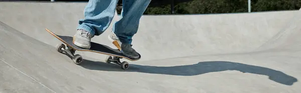 O jovem patinador desce sem esforço pela rampa de seu skate em um parque de skate ao ar livre em um dia ensolarado de verão. — Fotografia de Stock