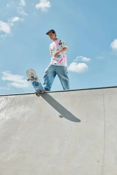 Joven skater boy montado con confianza monopatín por el lado de una rampa empinada en un parque de skate al aire libre soleado. - foto de stock