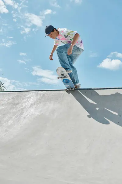 Ein junger Skater-Junge fährt an einem Sommertag selbstbewusst mit einem Skateboard die Seite einer Rampe in einem belebten Outdoor-Skatepark hinunter. — Stockfoto