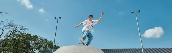 Un joven skater monta atrevidamente su monopatín encima de una rampa de cemento en un parque de skate al aire libre en un día de verano.. - foto de stock