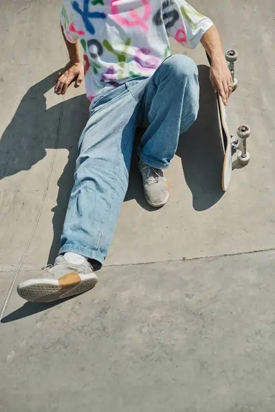 A young skater boy sits on his skateboard at a bustling skate park on a sunny summer day, contemplating his next thrilling move. — Stock Photo